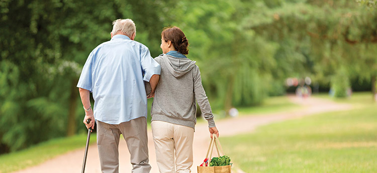 A caregiver is assisting an older man walk